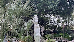 Un jardín con una estatua, una fuente y plantas en macetas.