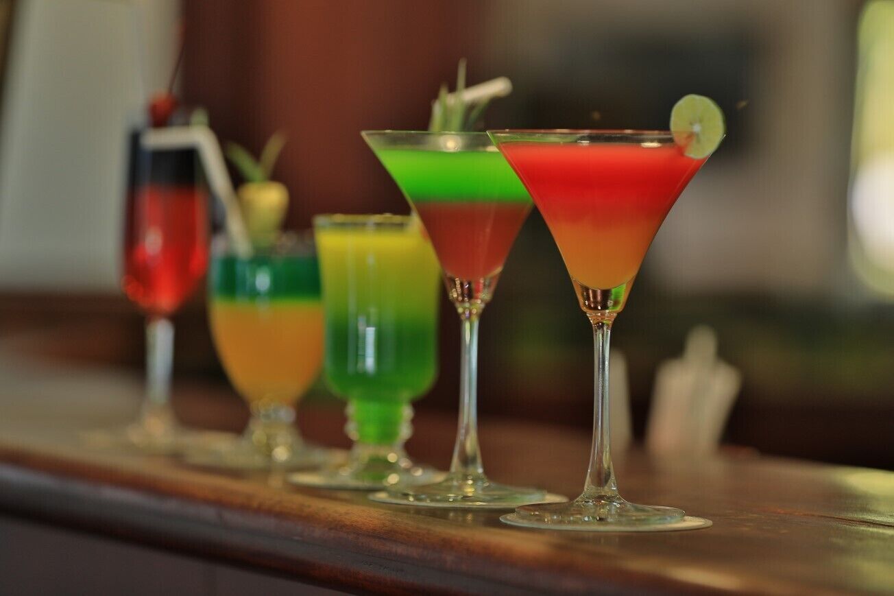 A row of colorful cocktails in martini glasses on a bar counter.