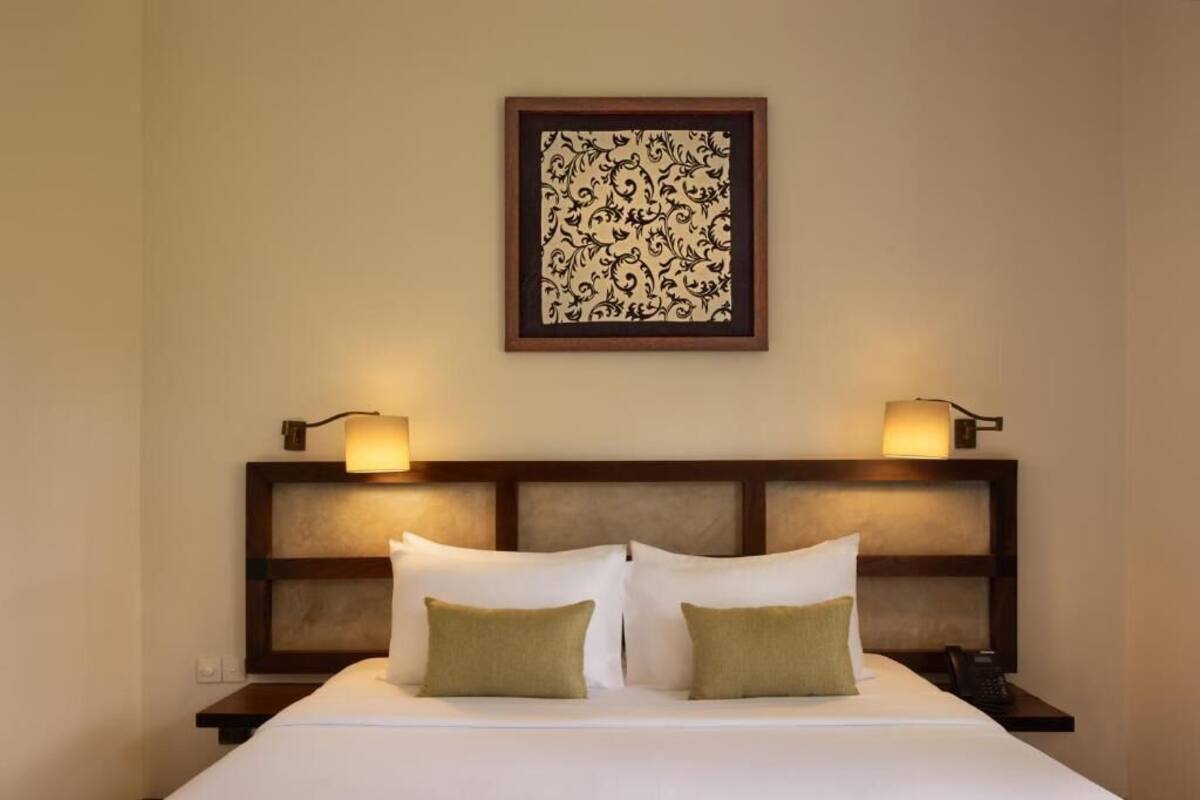 A neatly made bed with two pillows, a headboard with built-in lighting, and a framed artwork above.