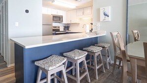 A modern kitchen with a central island, bar stools, and a dining table with chairs.