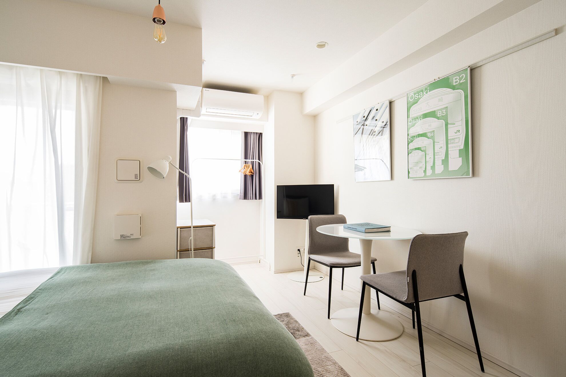 A modern hotel room with a bed, a dining area with chairs and a table, a TV, and artwork on the walls.