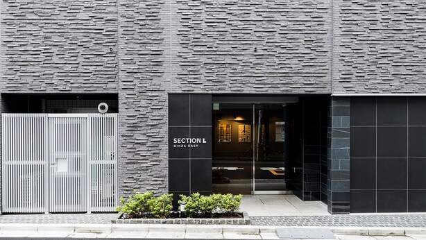 Eine moderne Gebäudefassade mit steinartiger Oberfläche und einem Schild, auf dem "SECTION L GINZA EAST" steht.