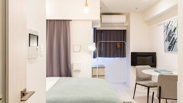 A modern hotel room with a bed, bedside table, desk, chair, and an air conditioning unit.