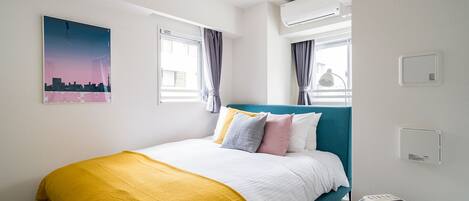 A modern bedroom with a teal headboard, a yellow throw blanket, and a cityscape painting on the wall.