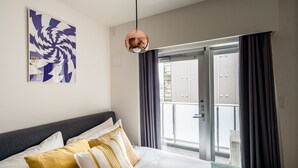Ein Hotelzimmer mit Bett, großem Fenster mit Vorhängen, Deckenlampe und einem Wandbild.
