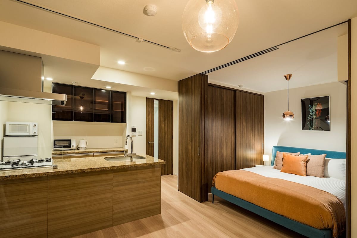 Quarto moderno com cama grande, roupeiro embutido e área de cozinha com micro-ondas e torradeira.
