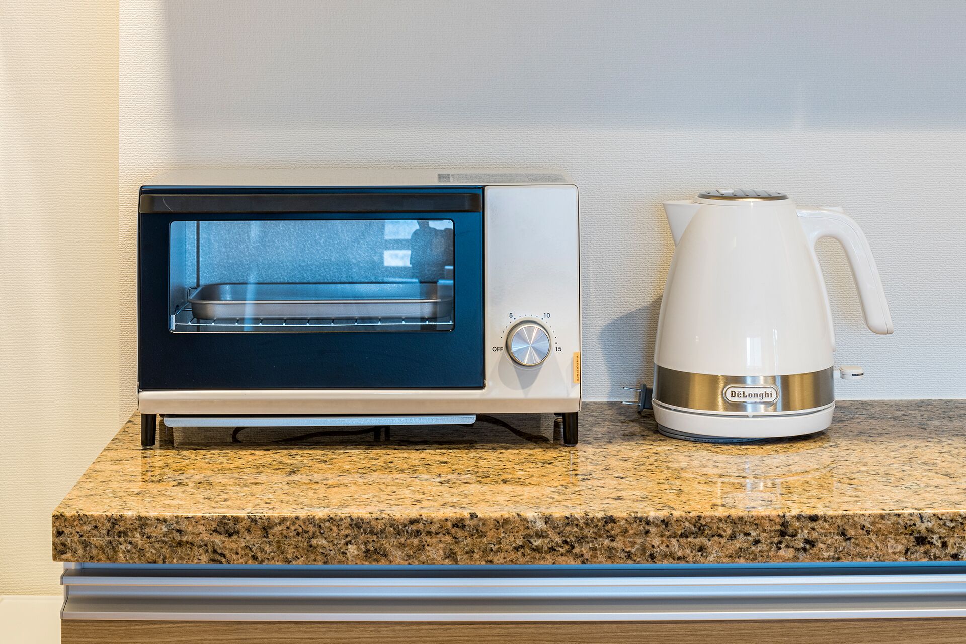 A kitchen with a built-in oven and a DeLonghi electric kettle on a granite countertop.