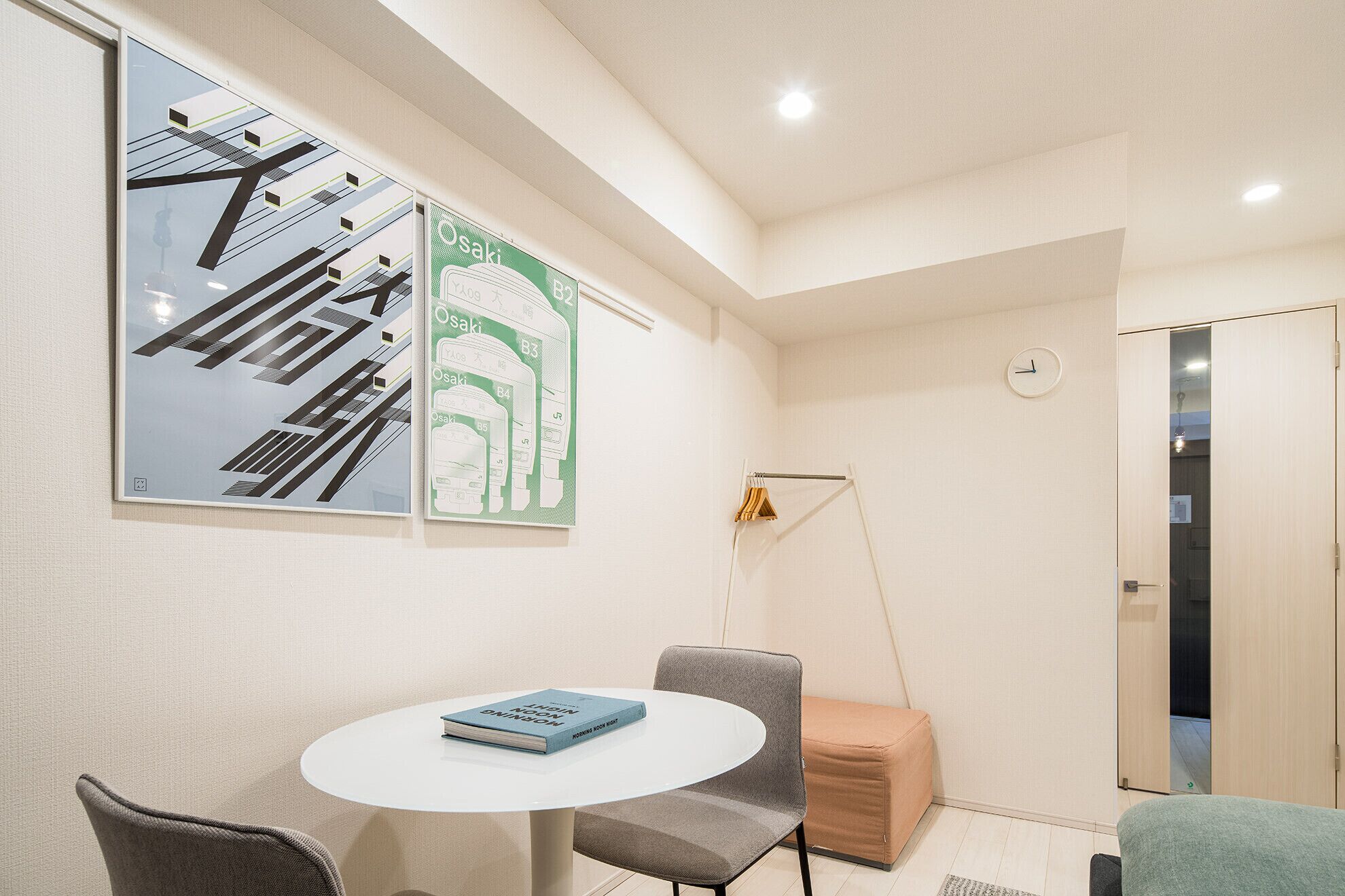 A modern room with a round table, two chairs, a bookshelf, and a wall-mounted clock.