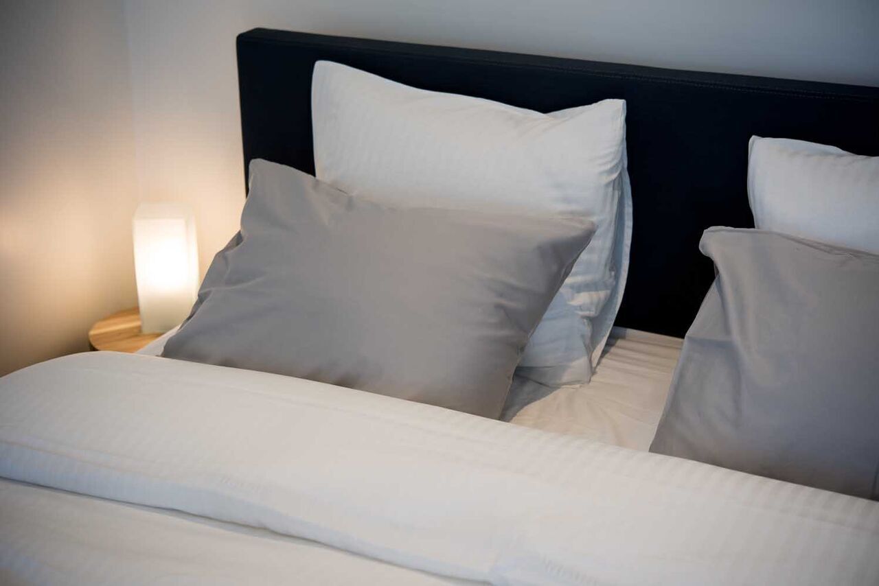 Een net opgemaakt bed met witte beddengoed en een donker hoofdbord.