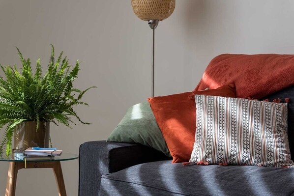 A modern living room with a grey sofa, a potted fern, and a floor lamp. - Studio Brussels Airport (Zaventem)