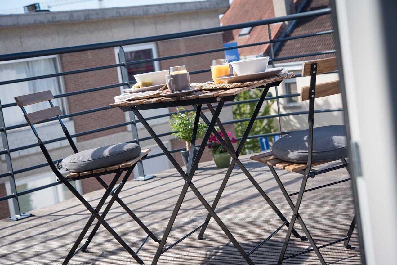 Un balcón con una mesa dispuesta para el desayuno, dos sillas y una planta en maceta.