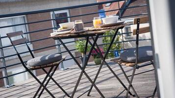 Un balcón con una mesa dispuesta para el desayuno, dos sillas y una planta en maceta.