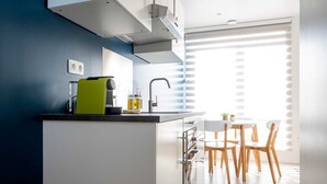 A modern kitchen with a built-in island, a sink, and a dining area with wooden chairs and a white table. - Studio Brussels Airport (Zaventem)