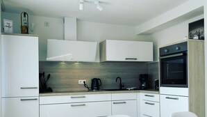A modern kitchen with white cabinetry, a built-in oven, and a coffee maker. - Modern apartment with prime, kitchen & WLAN (Rudolstadt)