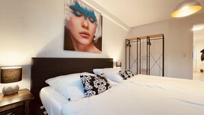A hotel room with a large bed, a nightstand with a lamp, a wall-mounted shelf, and a wardrobe with a mirror. - Modern apartment with prime, kitchen & WLAN (Rudolstadt)