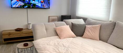 A modern bedroom with a large bed, a flat-screen TV mounted on the wall, a wooden side table, and a small round table.