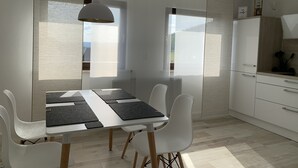 A modern kitchen with white cabinetry, a dining table with black placemats, and a pendant light. - Modern apartment with prime, kitchen & WLAN (Rudolstadt)