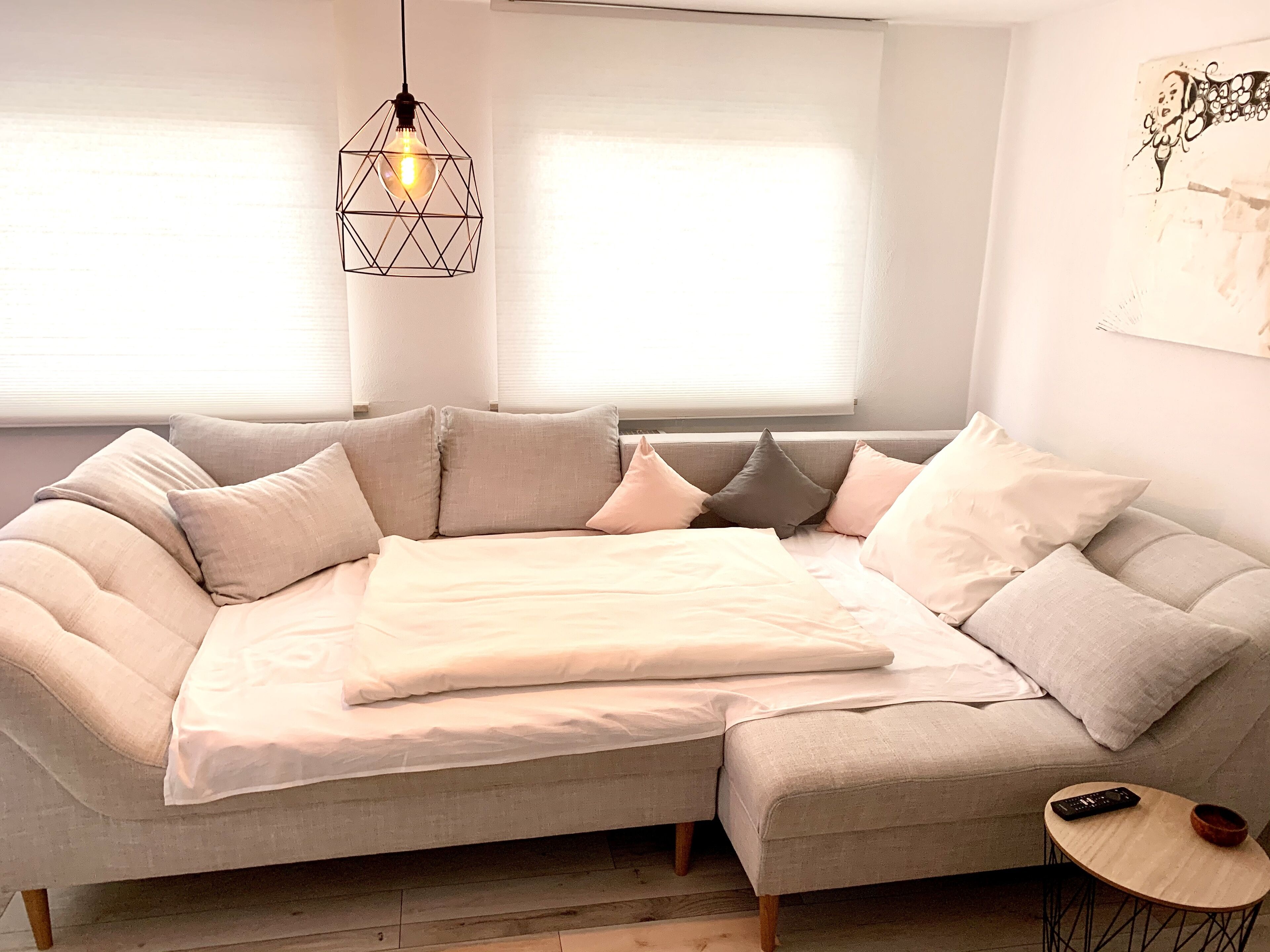 Una sala de estar moderna con un amplio sofá modular en forma de L, una pequeña mesa redonda de madera y una lámpara colgante.