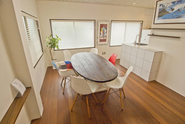 A compact kitchen with a dining area, featuring a round wooden table, white chairs, and a small white cabinet. - Step Pier (Onomichi)