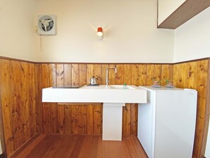A small kitchen with a white sink, wooden paneling, a kettle, and a refrigerator. - Step Pier (Onomichi)