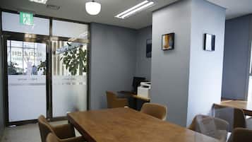 A hotel room with a wooden table, chairs, a desk with a computer, and a plant.