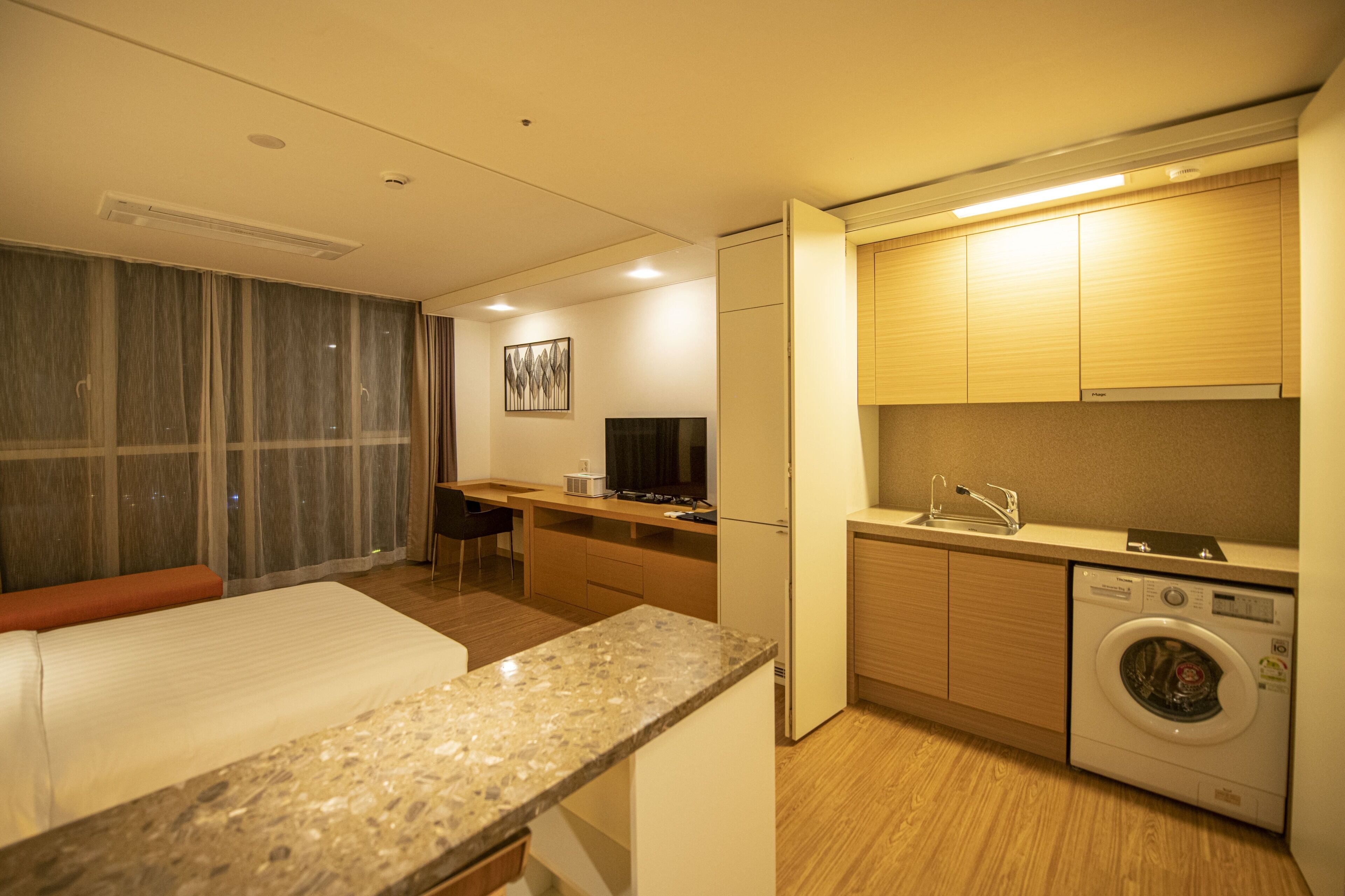A hotel room with a bed, a desk, a washing machine, and a television.
