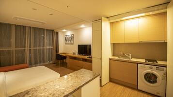 A hotel room with a bed, a desk, a washing machine, and a television.