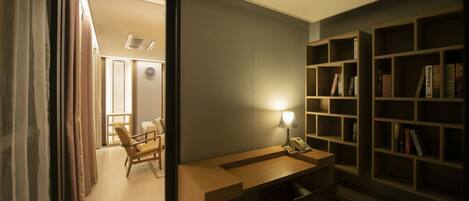 A hotel room with a desk, chair, bookshelf, and a view of the hallway.