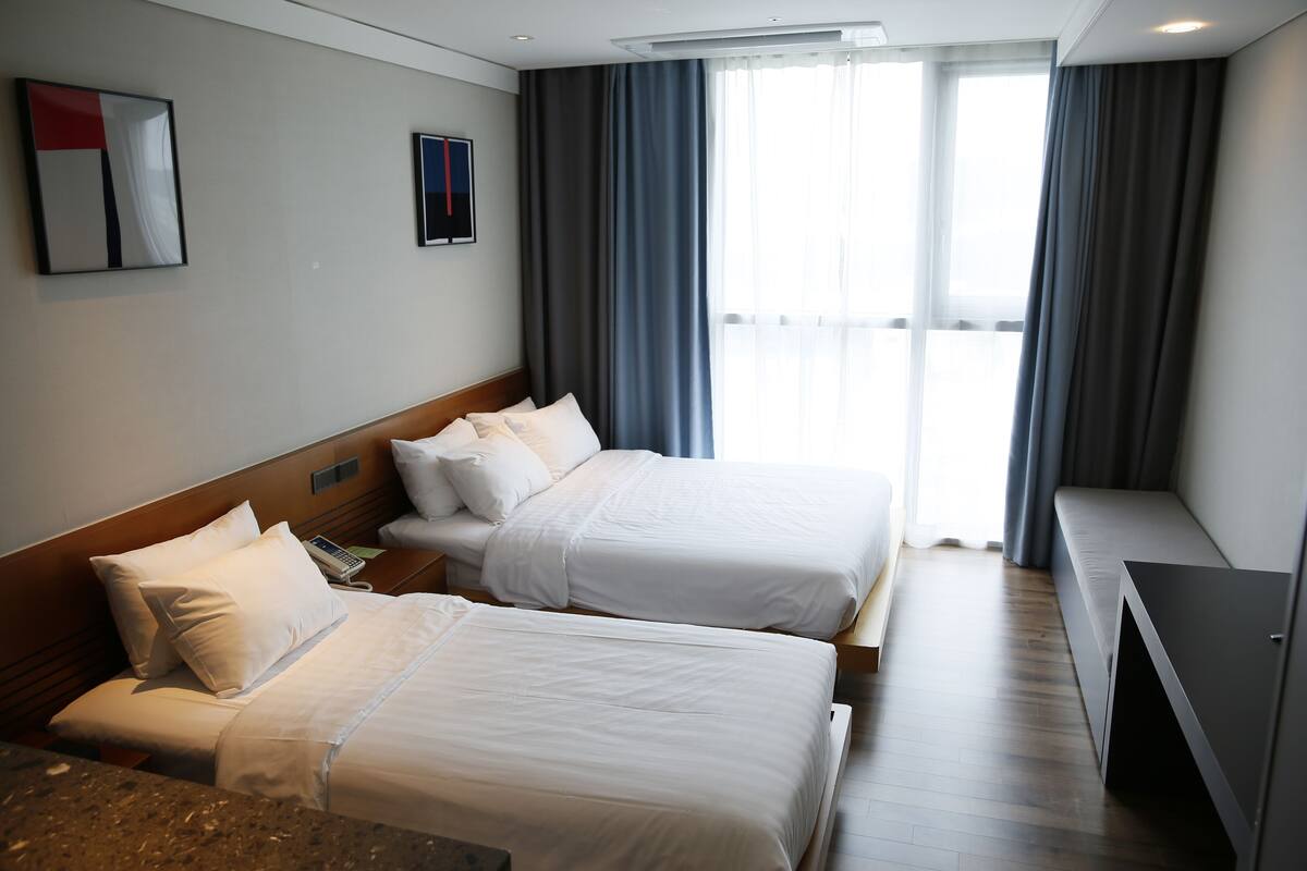 Une chambre d’hôtel avec deux lits, un bureau et une fenêtre avec des rideaux.