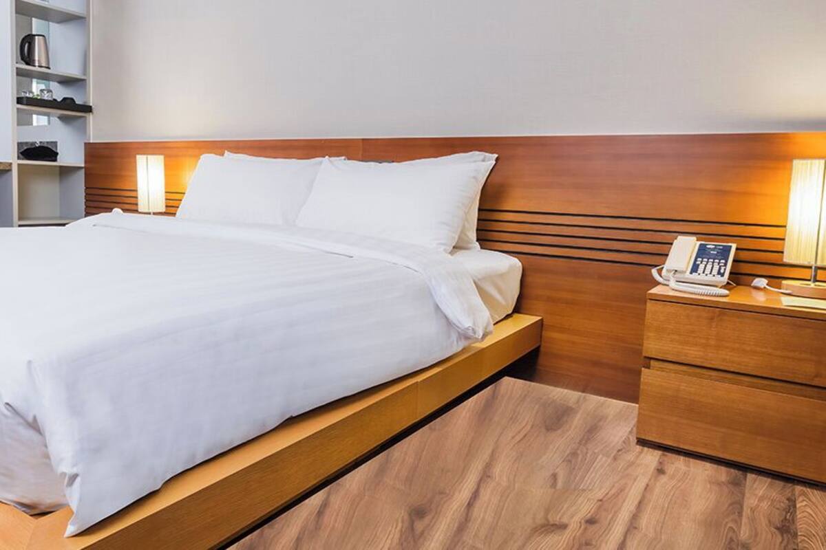 Une chambre d’hôtel avec un grand lit, une tête de lit en bois, des tables de chevet avec des lampes et un petit bureau avec un téléphone.