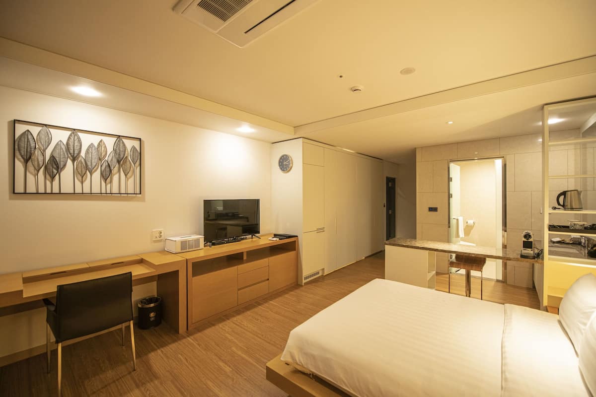 Une chambre d’hôtel moderne équipée d’un lit, d’un bureau avec un ordinateur, d’une chaise, d’une télévision et d’un coin cuisine.