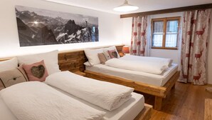 Une chambre avec deux lits, une tête de lit en bois, un grand tableau représentant un paysage de montagne, une fenêtre avec des rideaux et un luminaire au plafond.