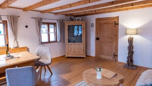 Une pièce chaleureuse avec des poutres en bois, une table à manger avec des chaises, un buffet avec une porte en verre et une lampe.