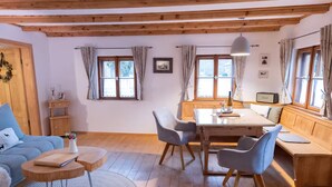 Une pièce chaleureuse avec un plafond en bois, une table à manger avec des chaises, un canapé et une fenêtre avec des rideaux.