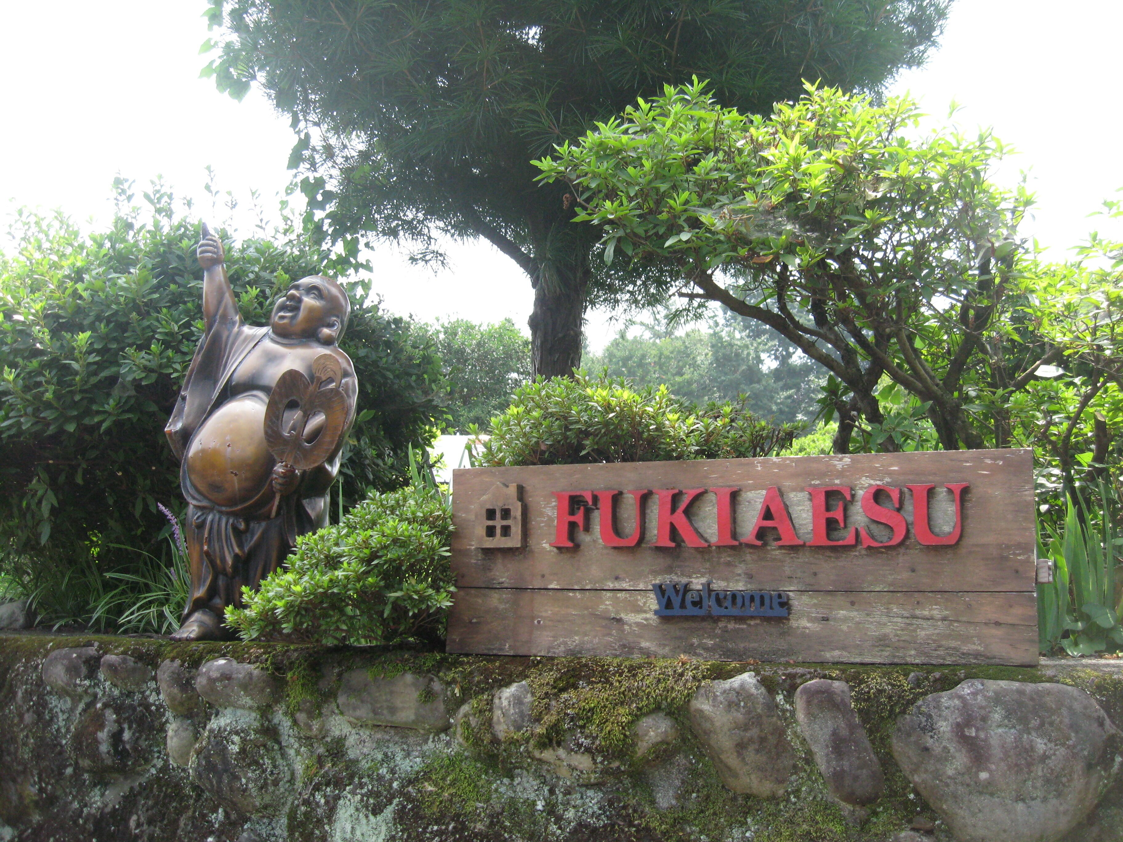 A welcome sign for FUKIAESU with a wooden backdrop and a sculpture.