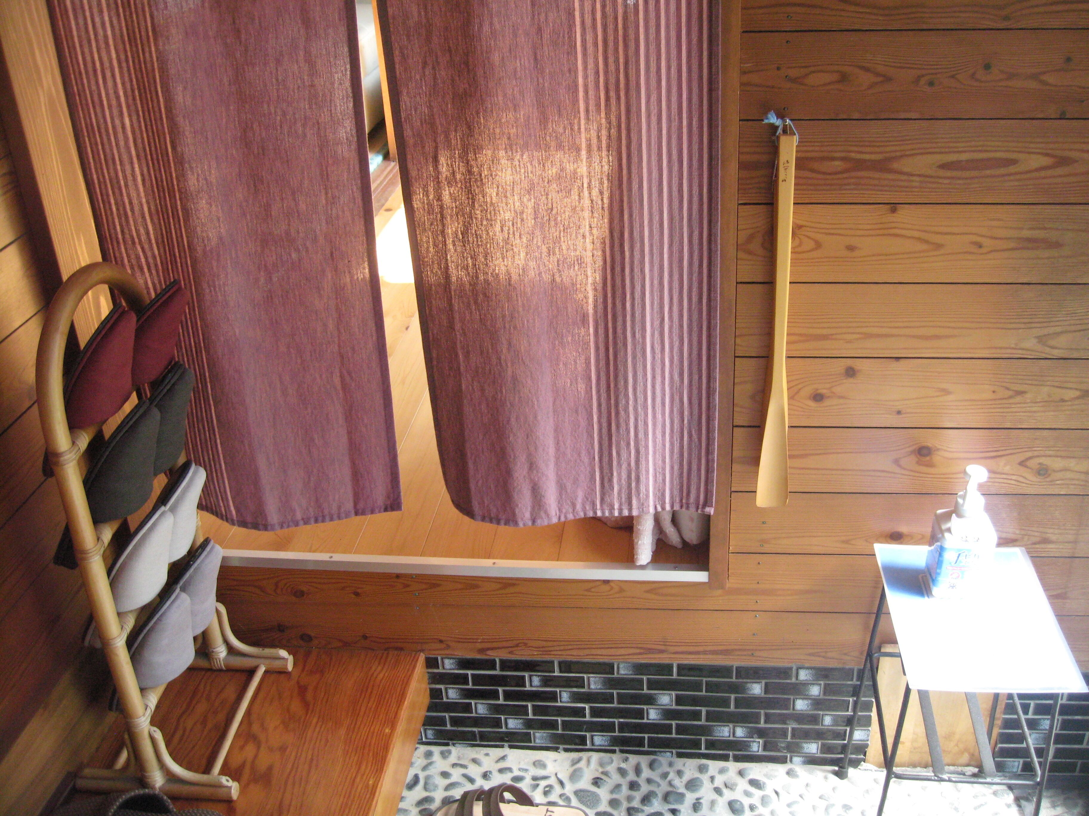 A wooden cabin interior with a wooden bench, a small table with a bottle, and a window with curtains.