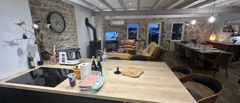 A modern kitchen with a central island, a stone wall, and a dining area with a view.