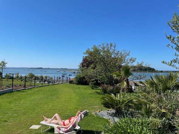 A woman sunbathing on a lawn chair with a view of the sea and boats.