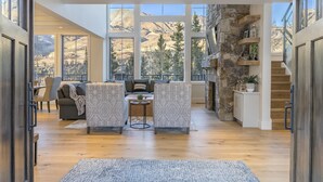 A spacious living area with a stone accent wall, large windows, and a cozy seating arrangement. - OVERLOOK HAUS- Mountain Oasis Overlooking San Sophia’s Ridge, Fire Pit & Hot Tub (Mountain Village)