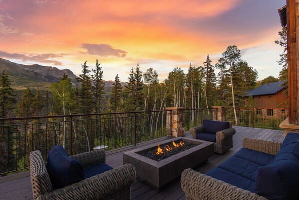A deck with outdoor furniture and a fire pit, overlooking a mountainous landscape.