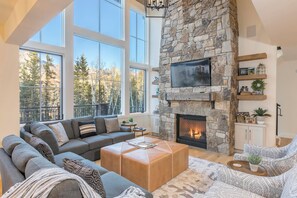 A spacious living room with a stone fireplace, large windows, and a cozy seating area.