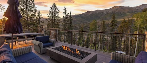 Una terraza con mobiliario exterior, un hogar para fogata y vista a las montañas.