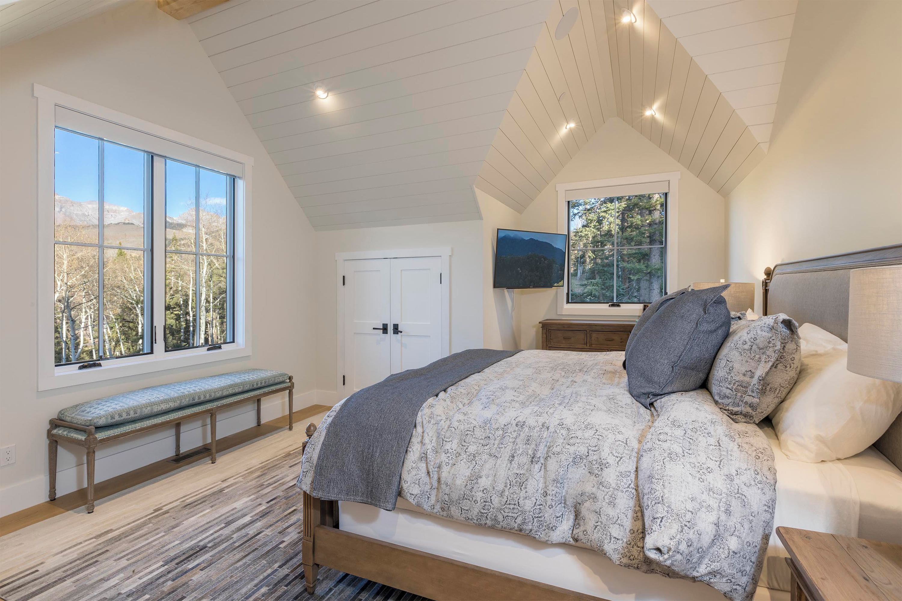 A bedroom with a large bed, a bench, a TV, and a door.