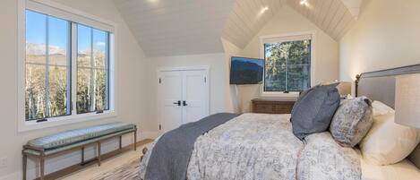 A bedroom with a large bed, a bench, a TV, and a door.