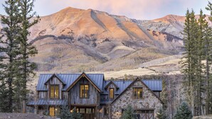 A rustic mountain lodge with a stone and wood exterior, large windows, and a metal roof. - OVERLOOK HAUS- Mountain Oasis Overlooking San Sophia’s Ridge, Fire Pit & Hot Tub (Mountain Village)