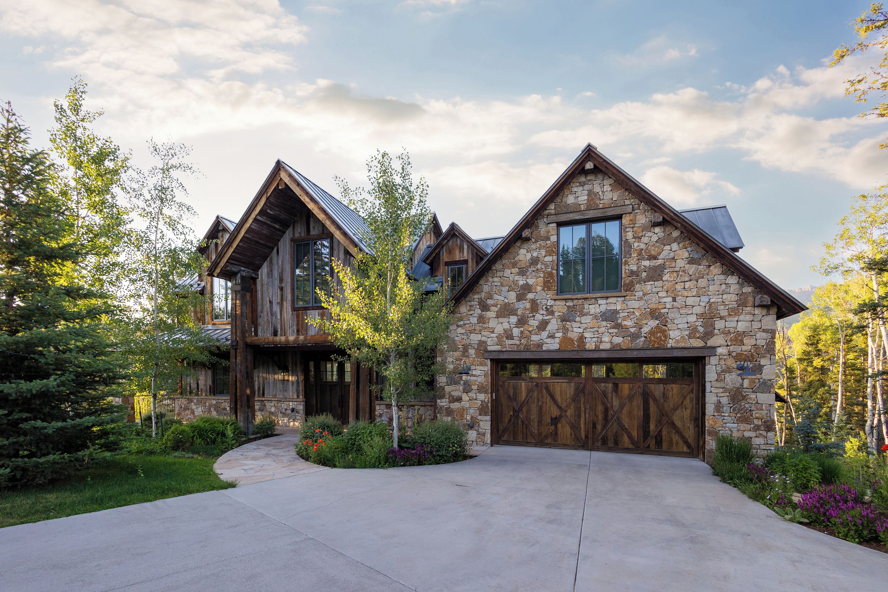 A large, two-story stone house with a prominent garage door and a well-maintained driveway.