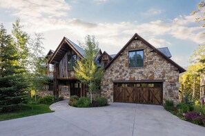 A large, two-story stone house with a prominent garage door and a well-maintained driveway.