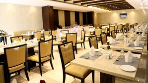 A hotel dining area with multiple tables and chairs, a flat-screen TV mounted on the wall, and a modern ceiling design. - YN Hotels (Bengaluru)