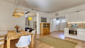 Una cocina moderna con armarios blancos, horno empotrado y zona de comedor con mesa y sillas de madera.