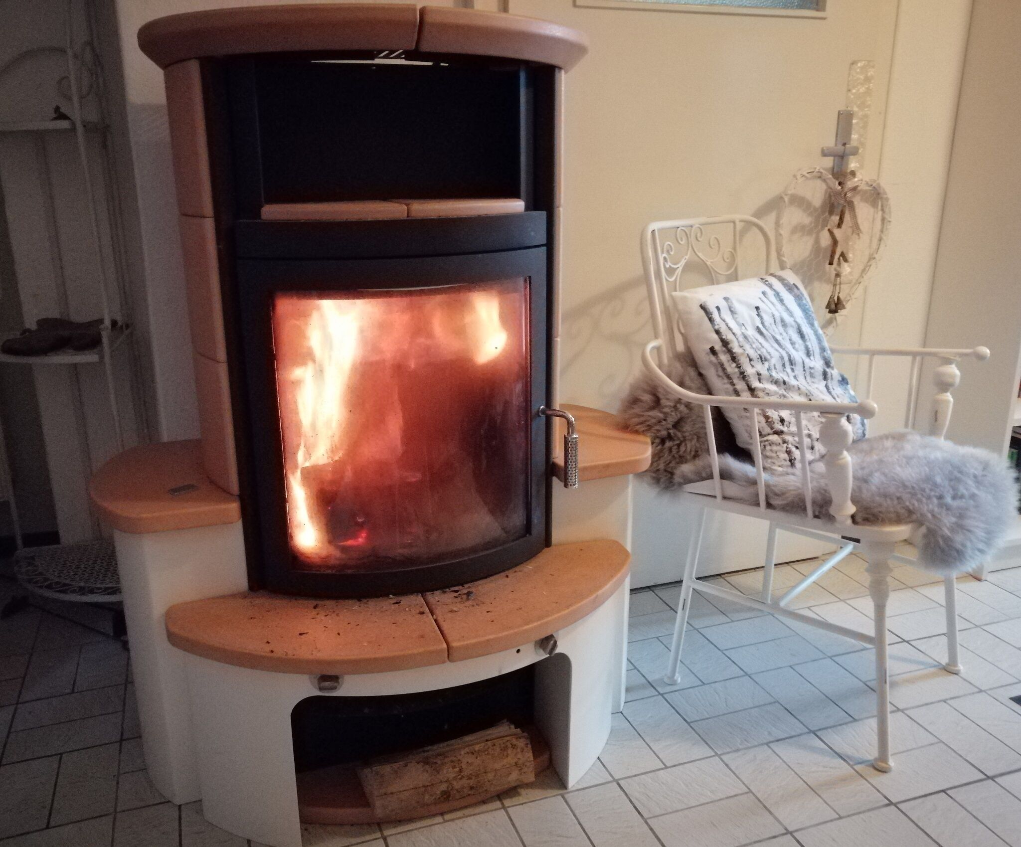 A wood-burning stove with a chimney, a white chair with a cushion, and a tiled floor.